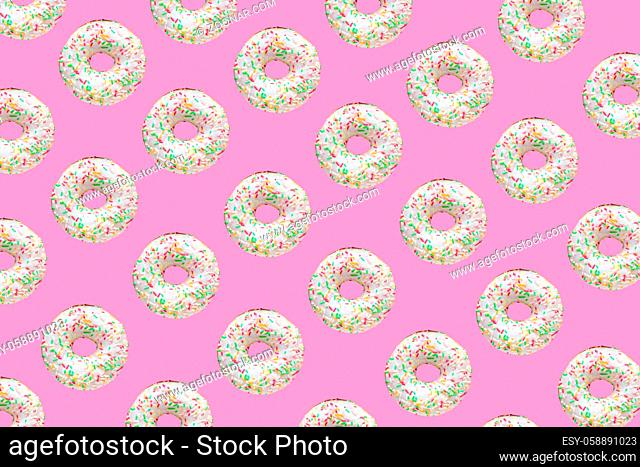 Pattern made of ring donuts with white glaze and clourful hundreds and thousands on pink background