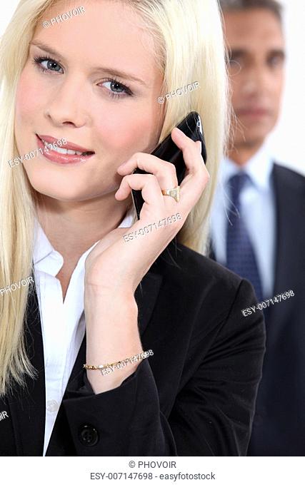 Smart woman using a cellphone as a male colleague watches in the background
