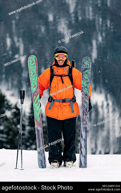 Smiling man standing with skis on snow in winter