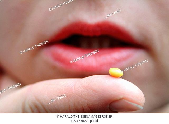 Yellow pill on a fingertip in front of a mouth