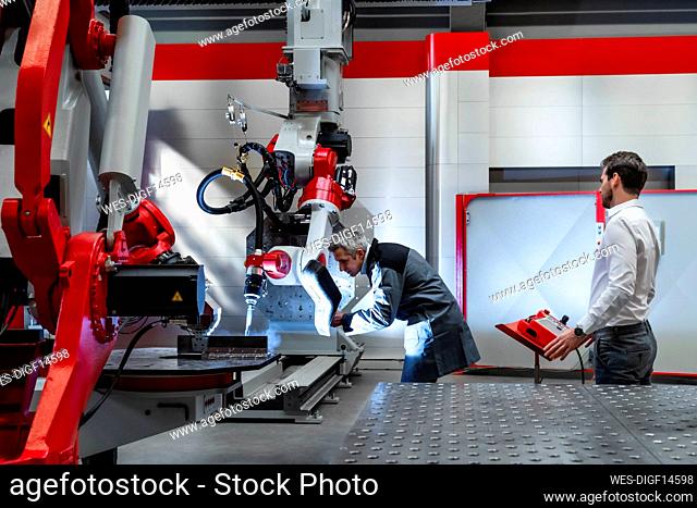 Mature man with welding helmet examining robotics in factory