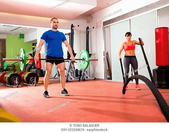 Crossfit gym weight lifting bar man woman battling ropes