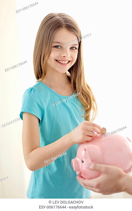 education, family, child and money saving concept - father holding piggy bank and child putting coins into it