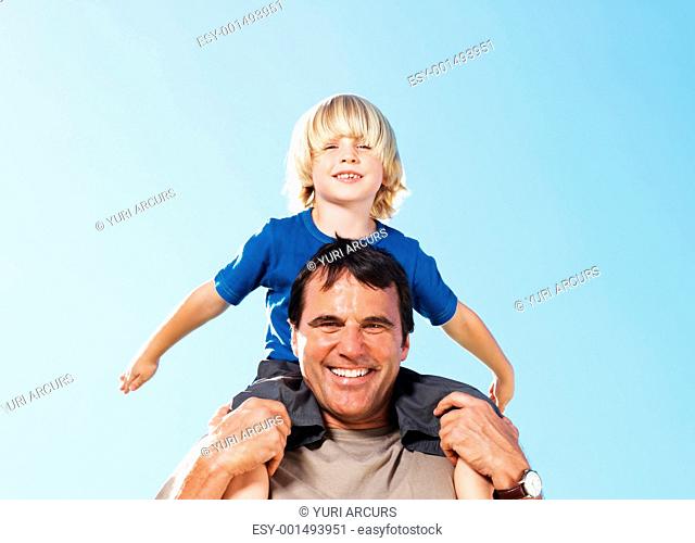 Portrait of handsome middle aged man carrying son on shoulders against sky