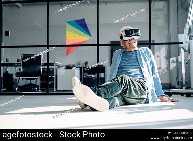 Businessman using virtual reality headset while relaxing on floor in office