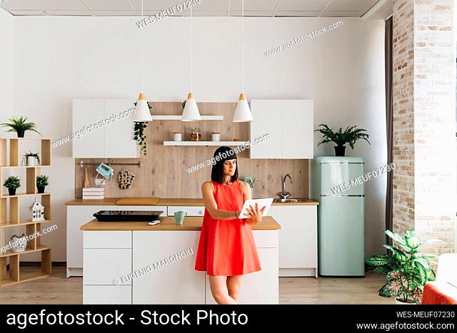 Freelancer woman using tablet PC standing by kitchen island at home