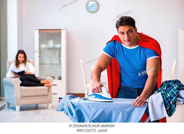 Super hero man husband ironing at home helping his wife