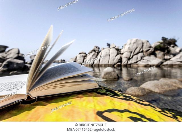 Opened book on towel at lonely rock beach