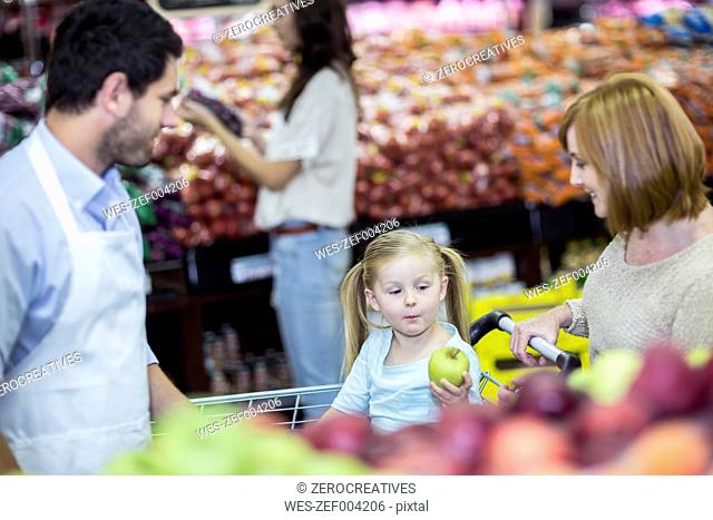 Shop assistant helping customers choosing fruits