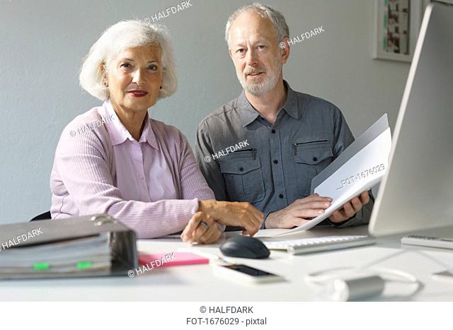 Portrait of confident business colleagues with documents at desk in office