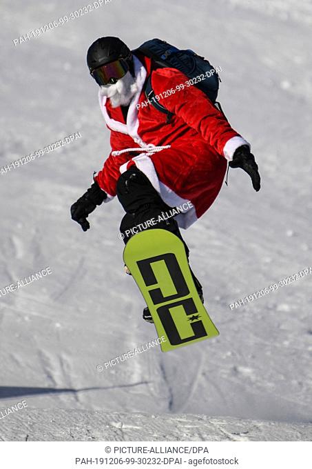 06 December 2019, Baden-Wuerttemberg, Feldberg Im Schwarzwald: A snowboarder disguised as Santa Claus jumps through the air at the start of the skiing season