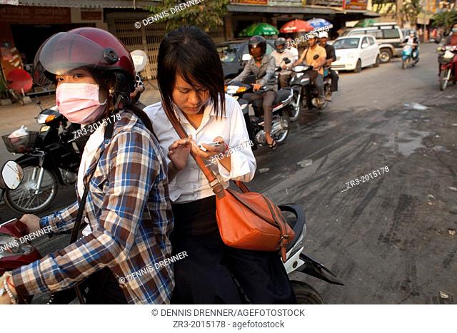A young woman text from the back of a motorbike in Phnom Penh, Cambodia