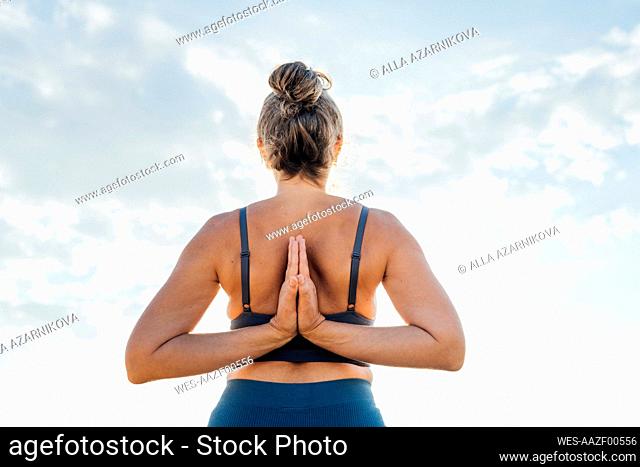 Woman practicing yoga with hands clasped in front of sky