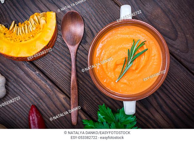 creamy pumpkin soup in a ceramic plate with a wooden spoon on the table, top view