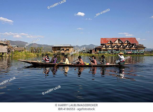 Local women in a wooden boat paddling on Inle Lake, stilt houses behind, Inle Lake, Shan State, Myanmar