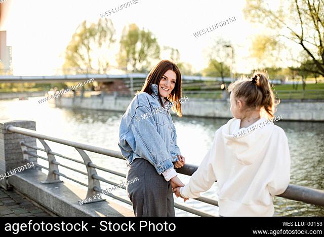 Smiling mother holding daughter's hand at embankment