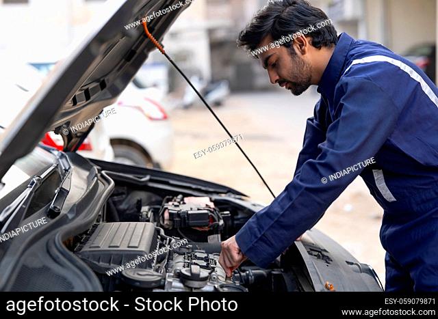 A YOUNG MECHANIC LOOKING AT A CAR BONNET AND REPAIRING IT