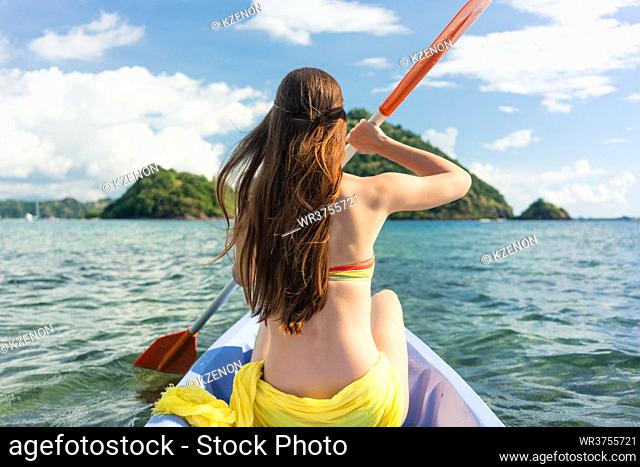 Rear view of a young woman paddling with a double-bladed paddle a canoe on the sea during summer vacation in Flores Island, Indonesia