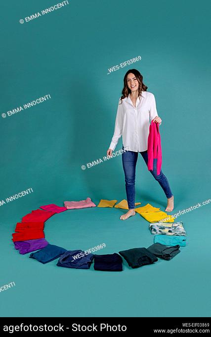 Smiling woman holding pink t-shirt stepping inside circle made of clothes against blue background