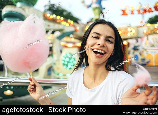 Close-up of beautiful woman holding cotton candy laughing in amusement park