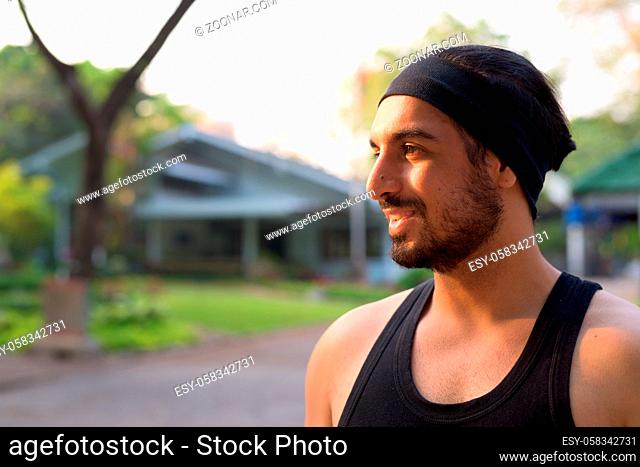 Portrait of young handsome bearded Indian man relaxing at the park