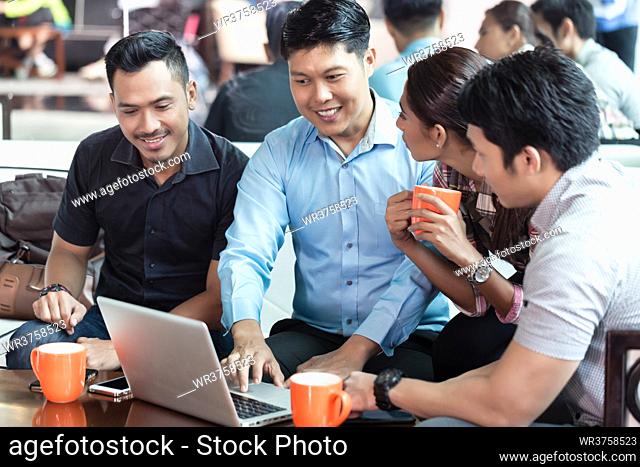 Team of four dedicated employees sitting in front of a laptop while working together at an innovative business project in a modern office