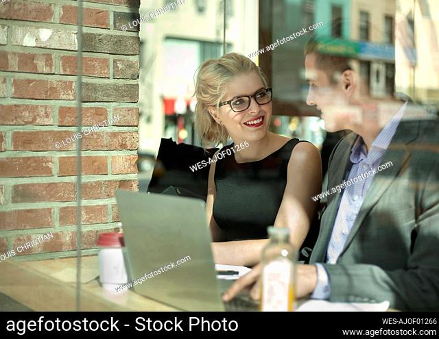 Smiling businesswoman looking at male colleague while working in cafe