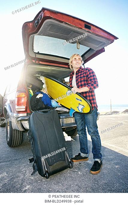 Caucasian man unloading surfboard from car hatch