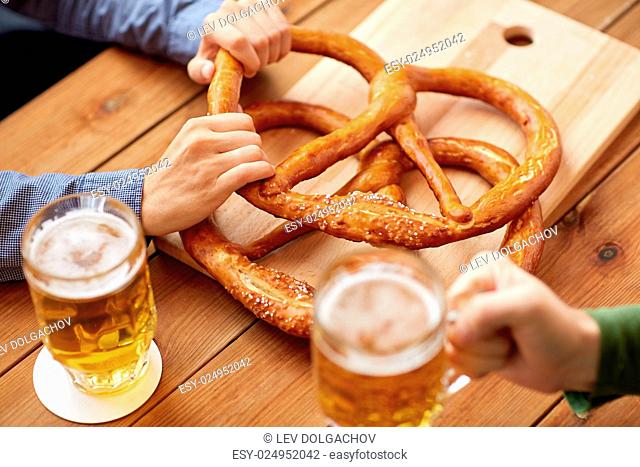 people, leisure and drinks concept - close up of men drinking beer with pretzels at bar or pub
