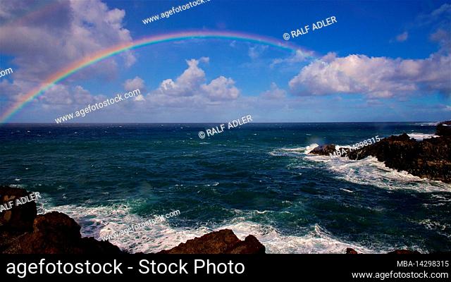 Canary Islands, Lanzarote, volcanic island, southwest coast, rugged volcanic coast, strong surf, sea caves, view of a rainbow over the sea, sea dark green