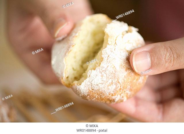 Human hand of young woman breaking bread fresh from oven