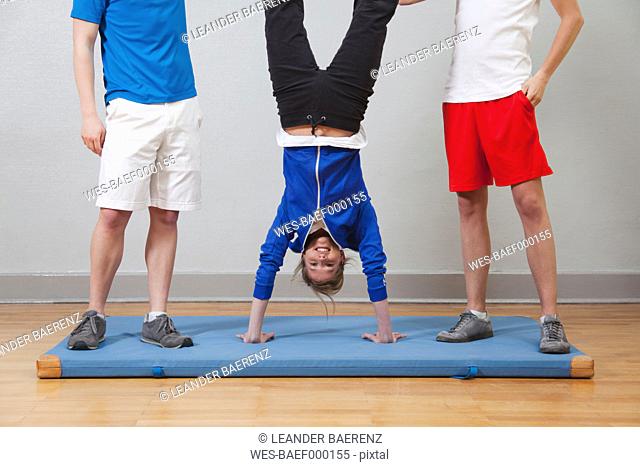 Germany, Berlin, Young woman practising handstand in school gym