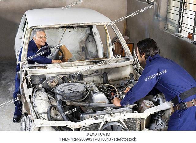 Auto mechanic with an apprentice repairing a car in a garage