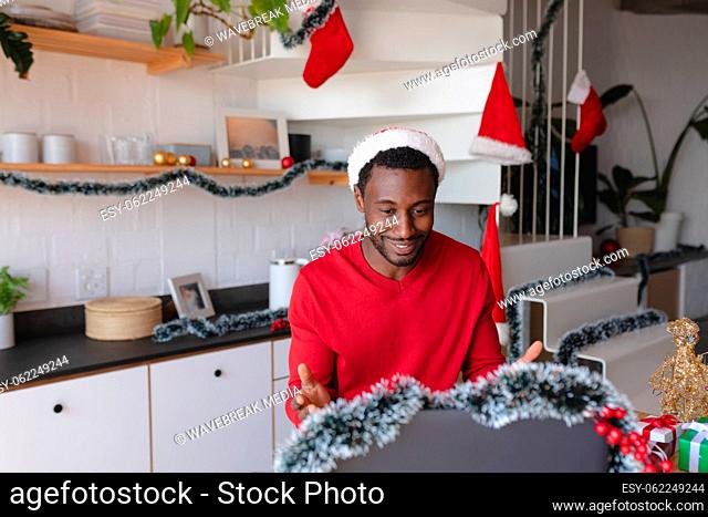 Happy african american man wearing santa hat, using laptop for video call