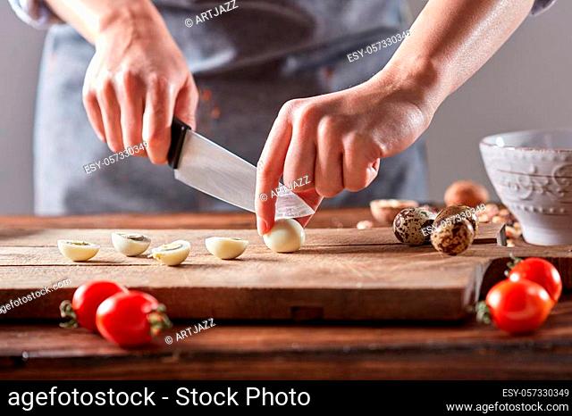On a wooden table, the hands of a woman cut quail eggs on an old wooden board. Step by step salad preparation