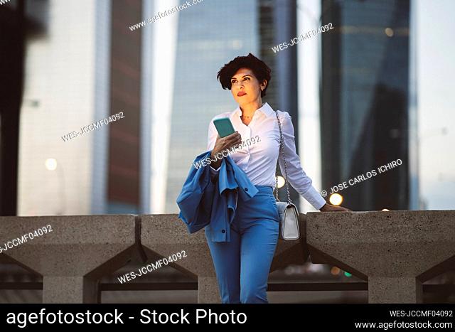 Female professional with smart phone standing by railing of bridge