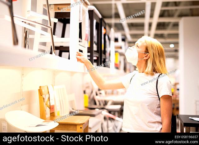 New normal during covid epidemic. Caucasian woman shopping at retail furniture and home accessories store wearing protective medical face mask to prevent...