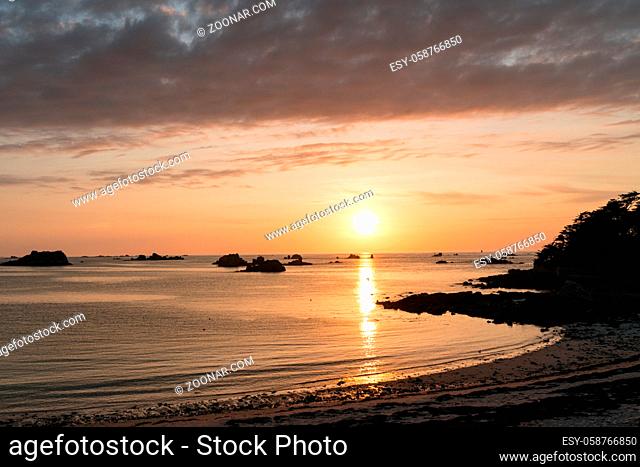 Horizontal view of a sunset over an idyllic bay and beach with a view of the ocean and rocky reefs under a colorful sky