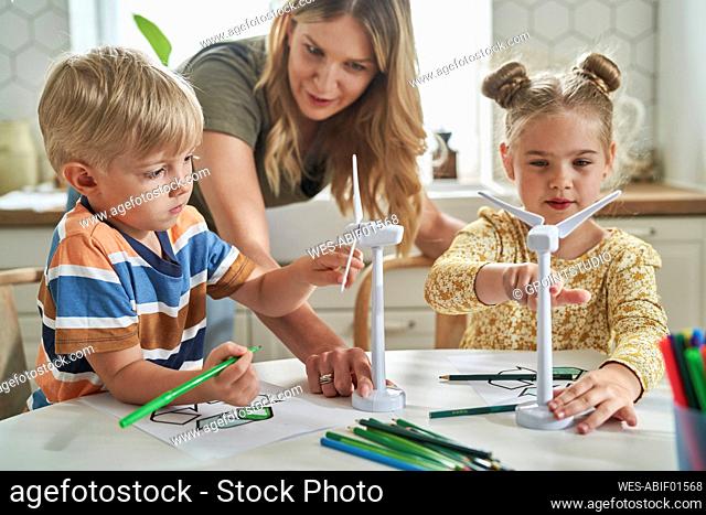 Mother teaching about wind turbine model to children at home