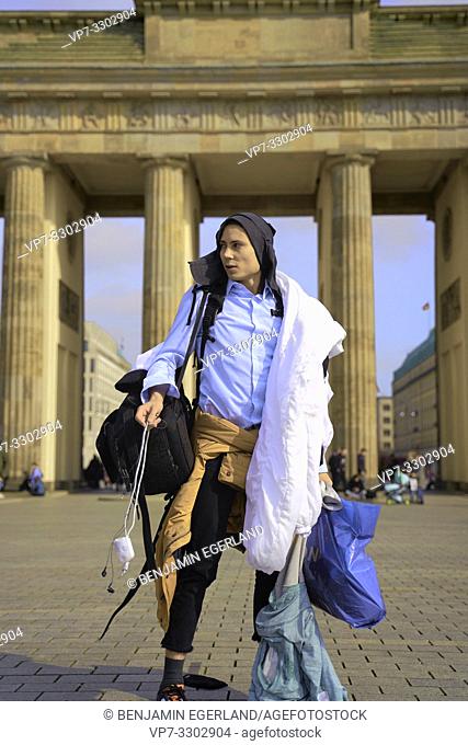 young tourist man, traveller, carrying too much baggage, in front of touristic sight Brandenburg Gate, in Berlin, Germany