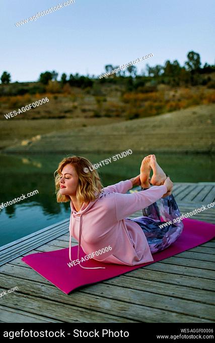 Young woman doing yoga on a jetty, bow pose