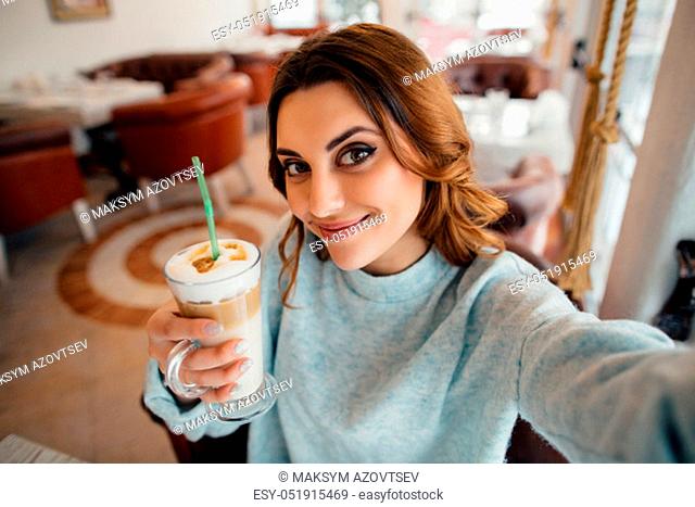 Beautiful girl making self portrait with coffee latte in cafe