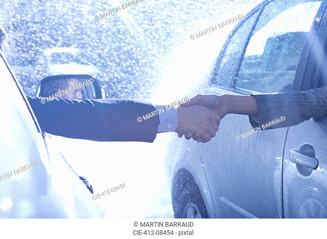 Businessman and businesswoman extending handshake from cars in rain