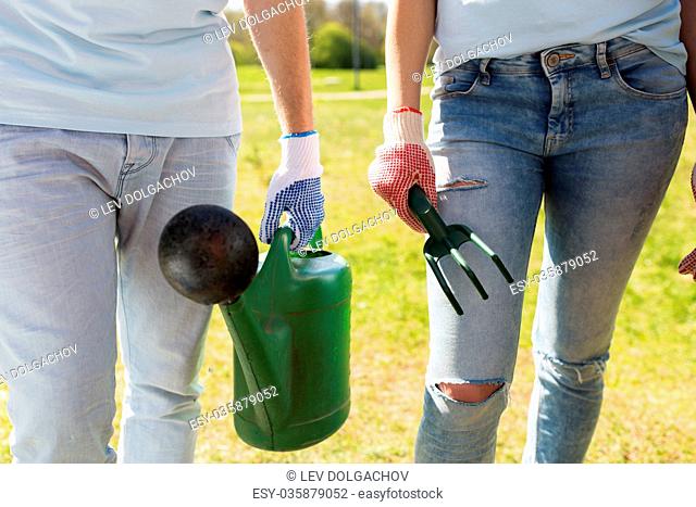 volunteering, people and gardening concept - couple of volunteers with watering can and weeding rake
