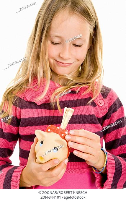 Blondes Mädchen steckt lachend einen Geldschein in ihr Sparschwein