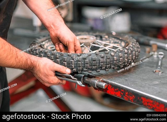 Mechanic repairing damaged motorcycle tire, in repair shop