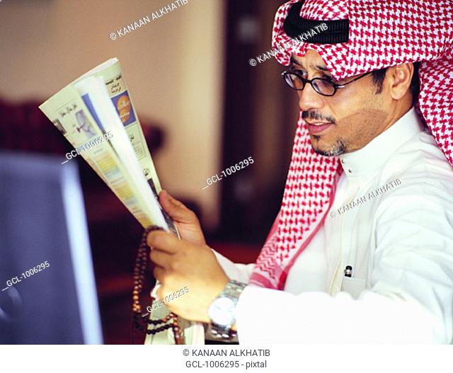 Saudi businessman reading Arabic newspaper and holding prayer beads