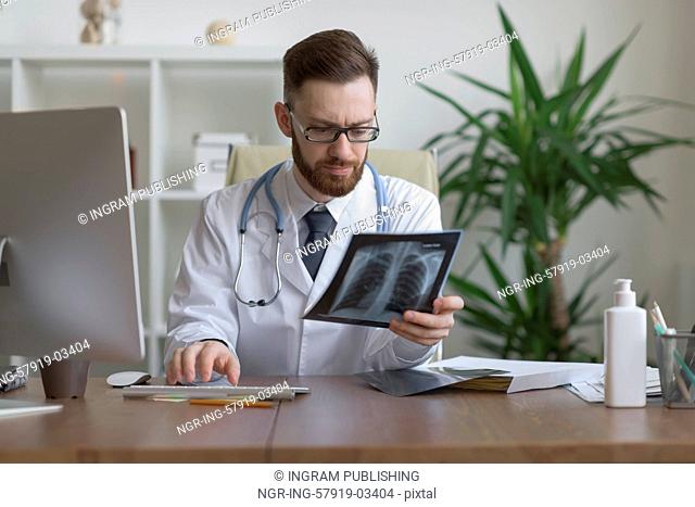 Thoughtful doctor holding chest and lungs xray in medical office