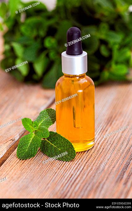 The small glass of essential oil and mint leaves on a wooden stand
