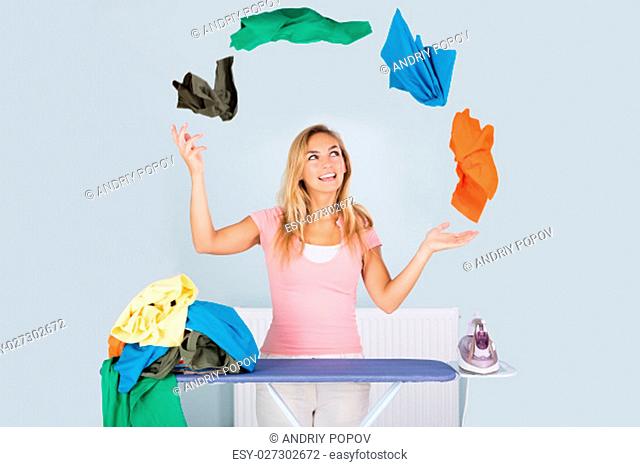 Young Smiling Woman Juggling With Colorful Clothes Near Ironing Board At Home